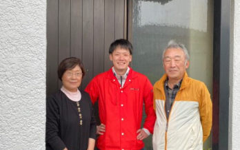 赤い制服を着た男性スタッフが夫婦と一緒に玄関先で笑顔で撮影した写真