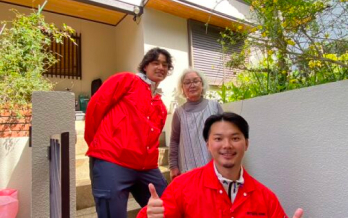 赤い制服を着た2人のスタッフが高齢女性と一緒に玄関先で笑顔で撮影した写真